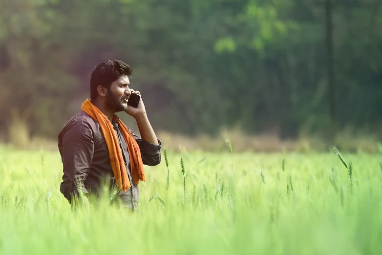 a man standing in a field talking on a cell phone, a picture, inspired by Thota Vaikuntham, shutterstock, hd movie photo, commercial shot, candid portrait photo, scene from live action movie