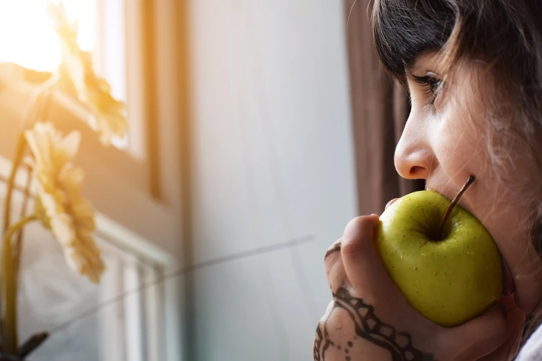 a woman eating an apple in front of a window, tiny girl looking on, promo photo, sentient fruit, up close picture