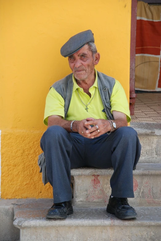 a man sitting on the steps of a building, a photo, by Juan Fernando Cobo, yellow cap, old man, heraldo ortega, he is very relaxed