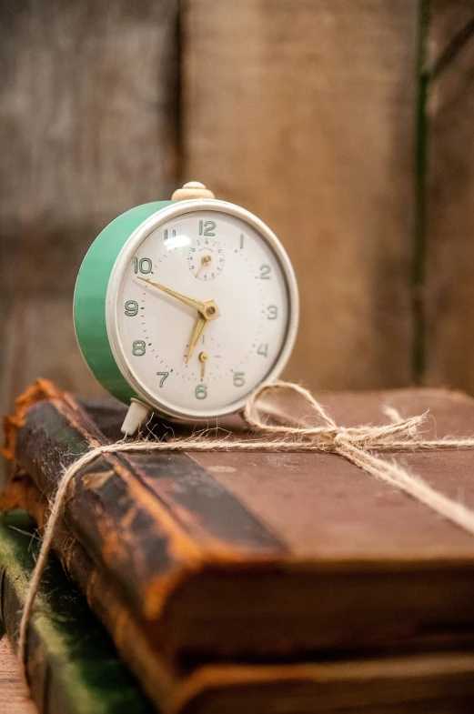 a clock sitting on top of a stack of books, greenish tinge, vintage inspired, promo, hay