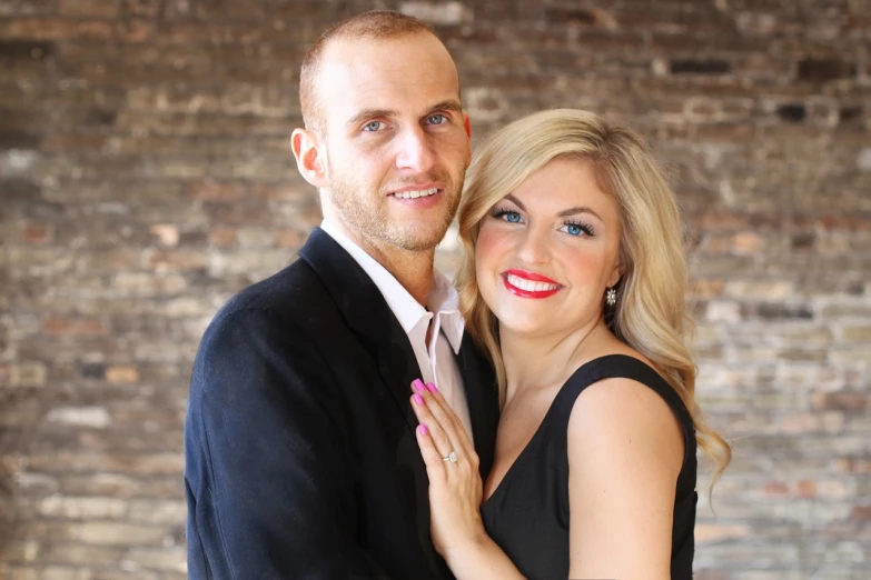 a man and woman posing for a picture in front of a brick wall, a portrait, by Kristin Nelson, elegant smiling pose, black and reddis, cory chase, closeup photo