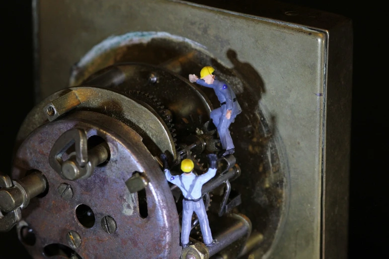 a couple of men standing on top of a metal object, a macro photograph, by Dave Allsop, flickr, open bank vault, repairing the other one, exposed inner gears, ho scale