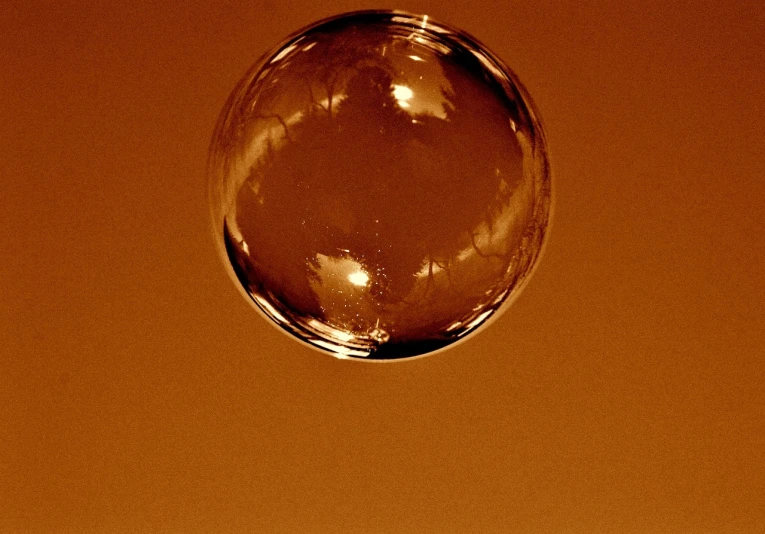 a close up of a glass ball on a table, a macro photograph, flickr, minimalism, brown water, soap bubble, in front of an orange background, sepia