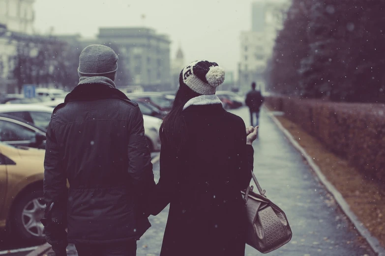 a man and a woman walking down a street in the snow, a picture, tumblr, romanticism, hand holding cap brim, on a rainy day, attractive girl, long distance photo