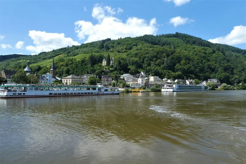 a group of boats floating on top of a river, by Rainer Maria Latzke, pixabay, hills in the background, germany. wide shot, vallejo, building along a river