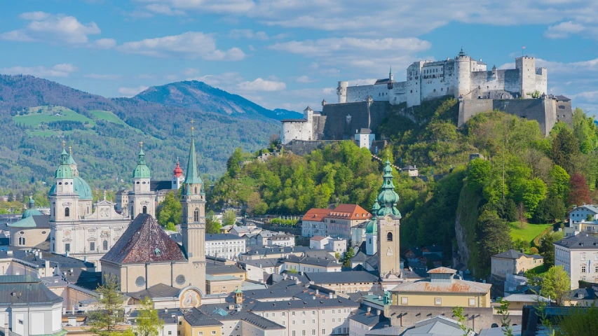 a large castle sitting on top of a lush green hillside, by Erwin Bowien, mountains and a huge old city, bright sunny day, whitewashed buildings, austria