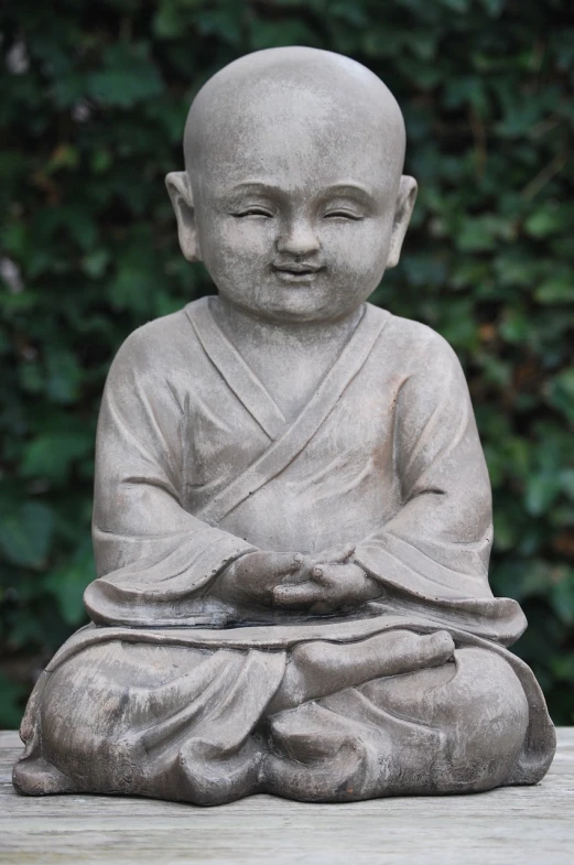 a statue sitting on top of a wooden table, inspired by Li Di, pixabay, sitting cross-legged, innocent smile, wearing simple robes, toddler