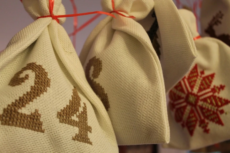 a couple of bags sitting on top of a table, a cross stitch, by Maksimilijan Vanka, pixabay, close up face detail, festive, ecru cloth, celebration of coffee products