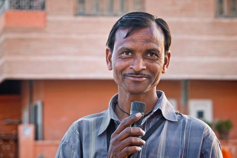 a man holding a microphone in front of a building, a picture, pixabay, samikshavad, friendly face, anthropologist, india, in 2 0 1 2