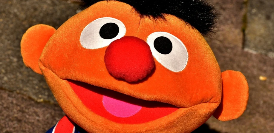 a close up of a stuffed animal wearing a shirt, a cartoon, flickr, orange fuzzy muppet, his nose is a black beak, [[[[grinning evily]]]], disney cartoon face