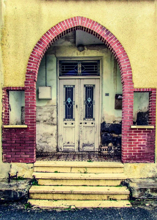 a yellow and red brick building with a white door, a photo, pixabay, art nouveau, white stone arches, abandoned photograph, ((oversaturated)), weathered