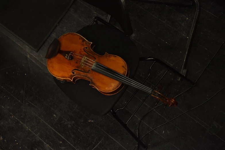 a violin sitting on top of a black chair, flickr, phone photo, on an empty stage from above, well worn, traditional