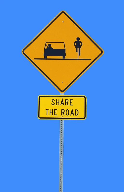 a yellow street sign sitting on the side of a road, a picture, pixabay, riding a bike, 2 people, shag, facebook post