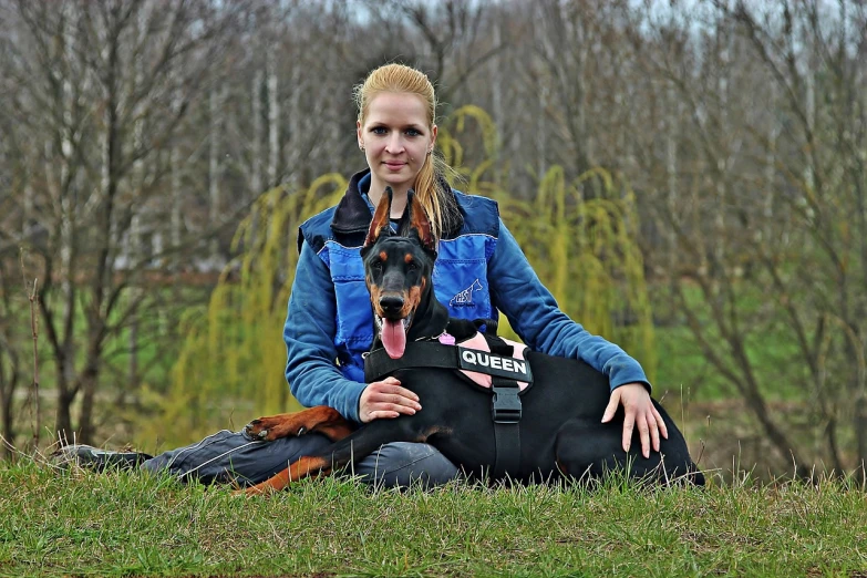 a woman sitting on the ground with a dog, a photo, pixabay, vest, huge, german, highly technical