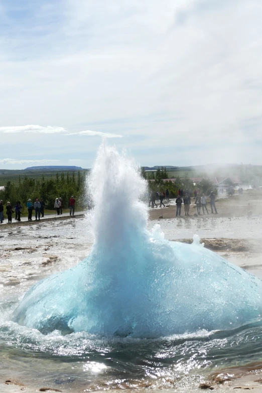 a group of people standing around a blue geyse, by Ejnar Nielsen, pexels, wave of water particles, an ice volcano, usa-sep 20, round-cropped