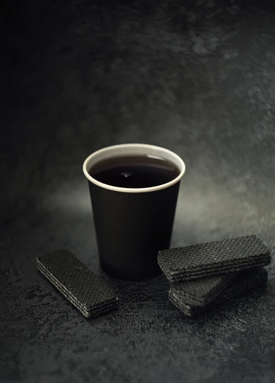 a cup of coffee and some cookies on a table, by Adam Chmielowski, black paper, paper cup, paul barson, tsukasa dokite