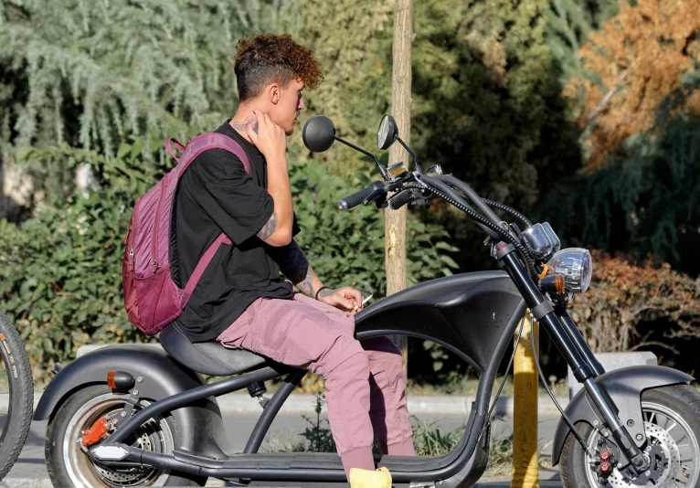 a man sitting on a motorcycle talking on a cell phone, pixabay, vanitas, 14 yo berber boy, side view profile, he has short curly brown hair, wearing a baggy