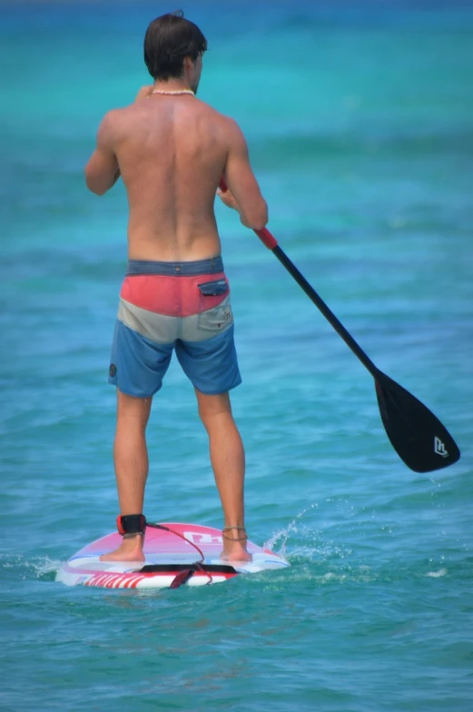 a man stands on a surfboard and paddles himself in the water