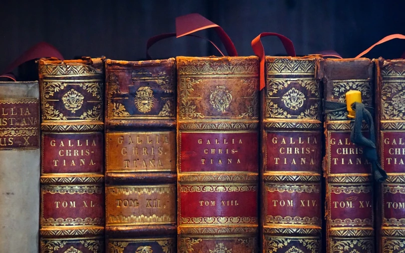 a set of vintage books are adorned with gold and red trim