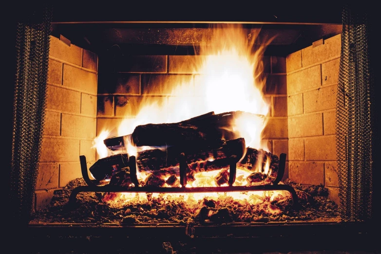 an open fireplace with bright yellow flames and a man made wooden bench