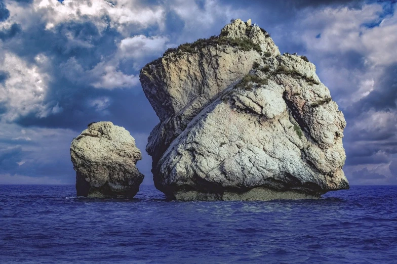 two large rocks floating in the ocean with cloudy sky above