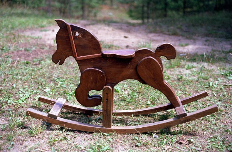 wooden rocking horse on grassy area with dirt and trees