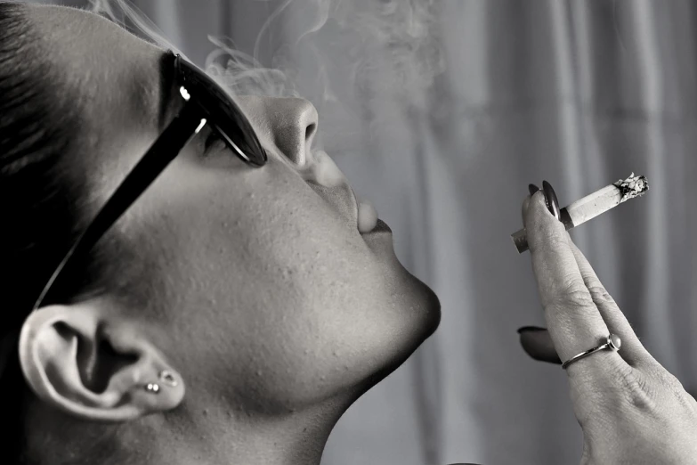 the woman is wearing sunglasses while smoking a cigarette