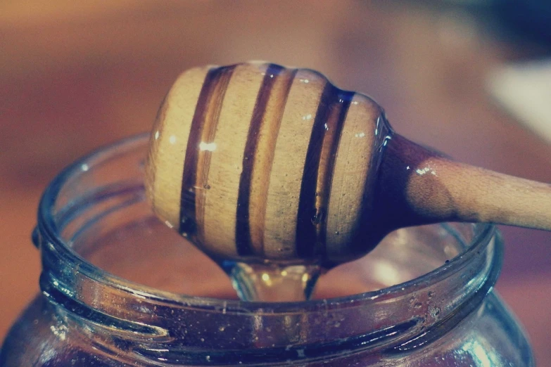 a honey dripping into a jar with a wooden spoon