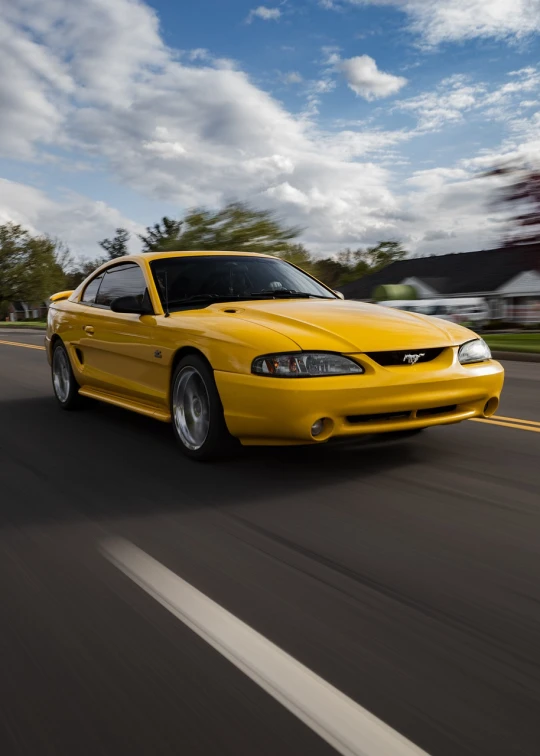 the yellow mustang mustang is driving down the street