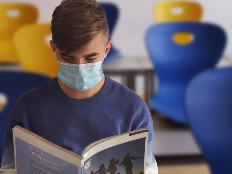 a young man reading a book wearing a mask