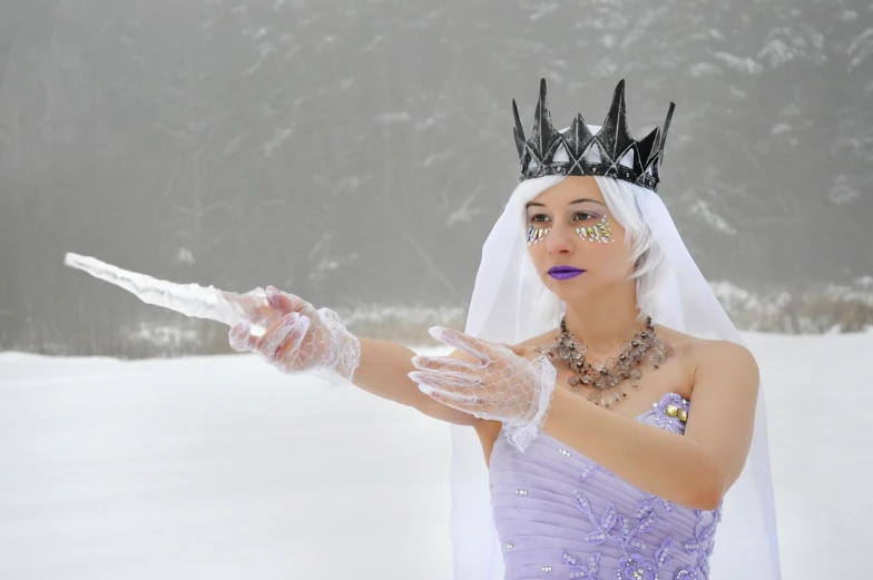 a woman wearing a dress and veil holding a wand in the snow