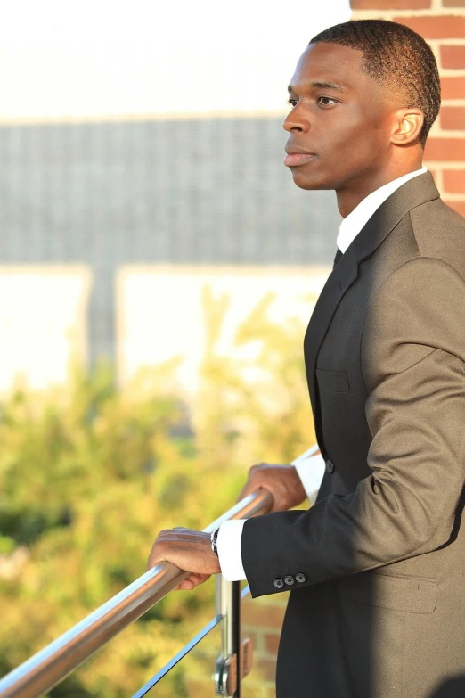 an african american businessman in a black suit leaning against a railing