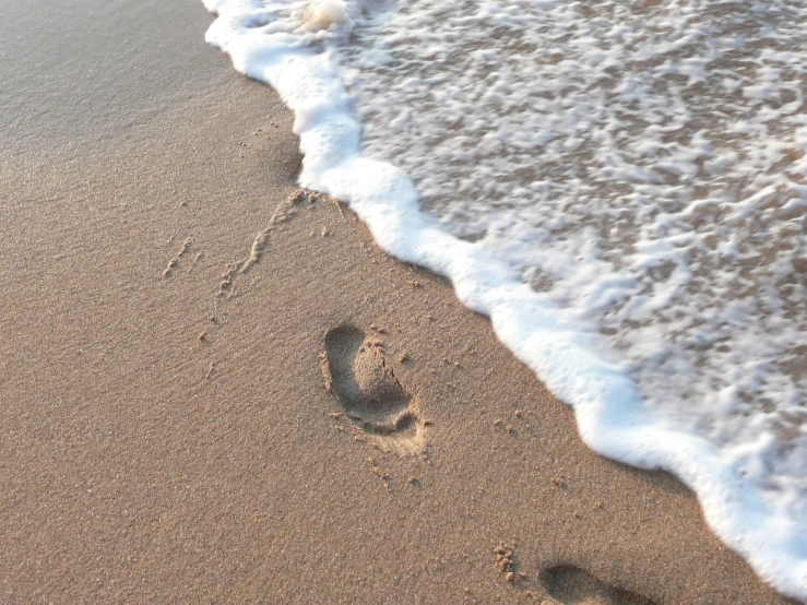 a persons feet imprint in the sand by a body of water