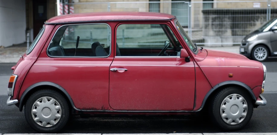 a small red car sitting on the side of the road