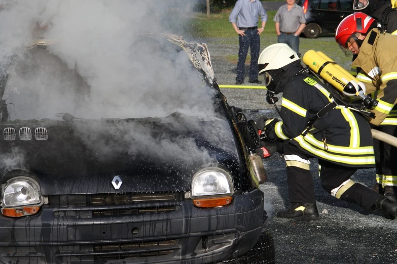 firefighters wearing helmets are trying to extinguish the fire from a car