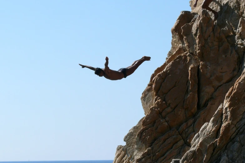 a person on a surfboard jumps off a cliff into the water