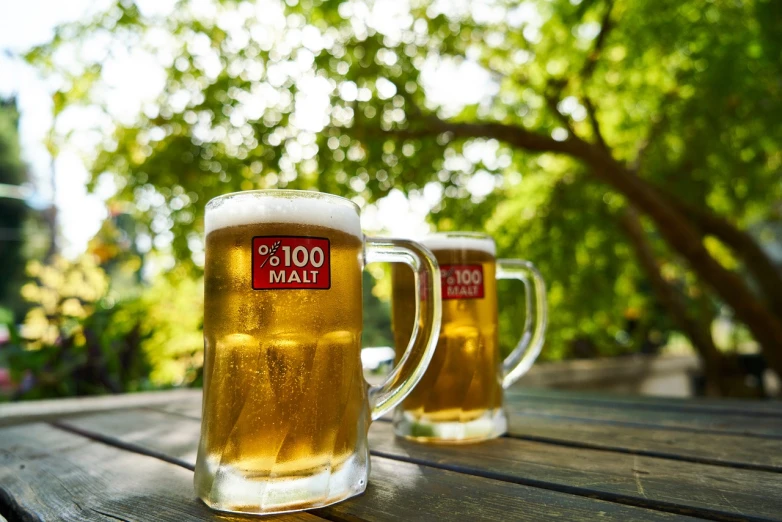 two mugs filled with beer sitting on top of a wooden table