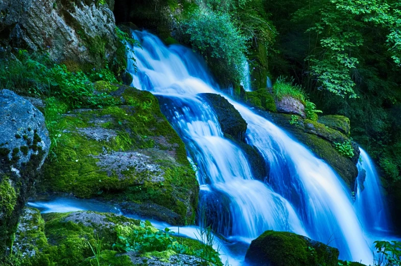 a large waterfall flowing over some rocks next to a green forest