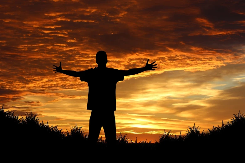 a man is standing in the sunset holding his hands out