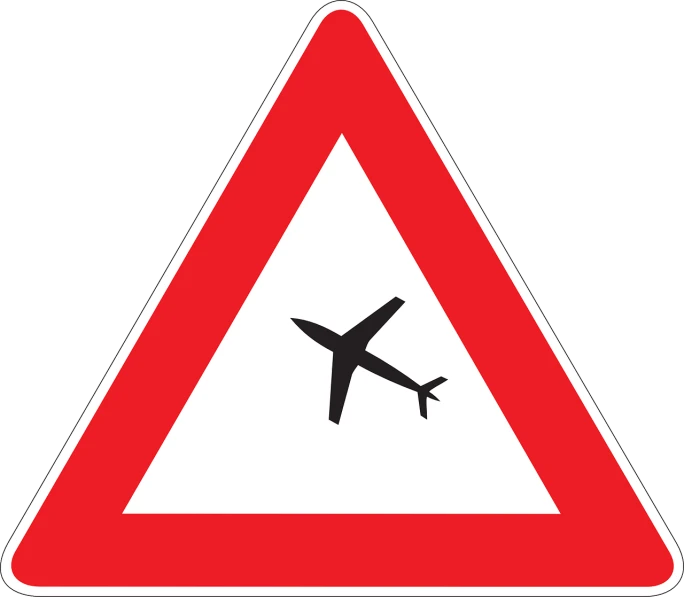 an airplane is in the sky, above a red triangular sign