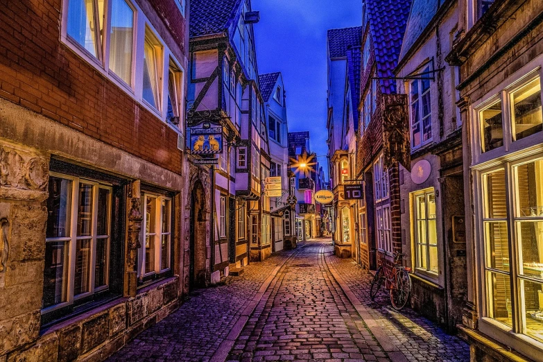 a narrow bricked street has an old clock tower on one side