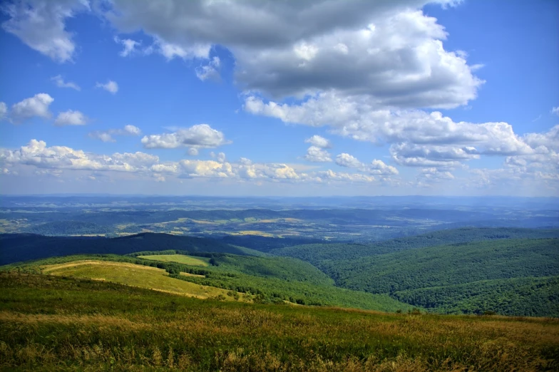 a view from the top of a mountain with beautiful green hills and rolling clouds