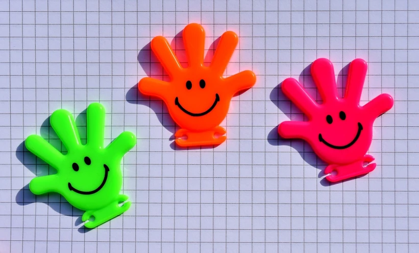 three plastic hand - shaped objects with faces, on top of a tile background