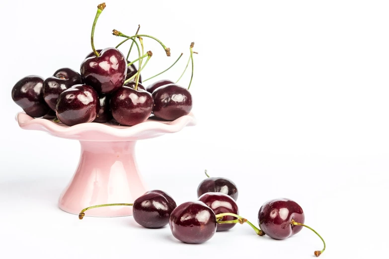 an oval pink vase full of cherries and stems on the floor