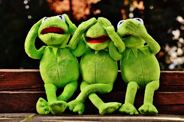 three kermie frogs hugging each other on a bench