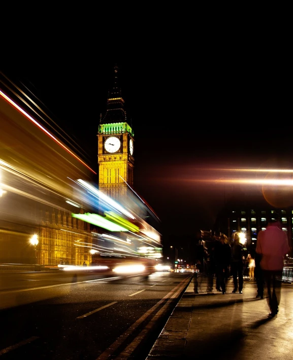 people walking on the sidewalk in front of a large clock tower