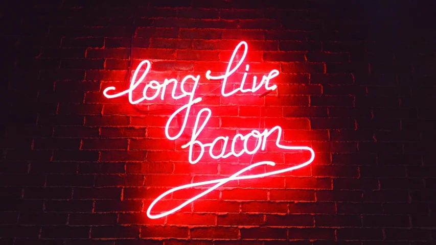 a red brick wall has a neon sign saying long time aaron