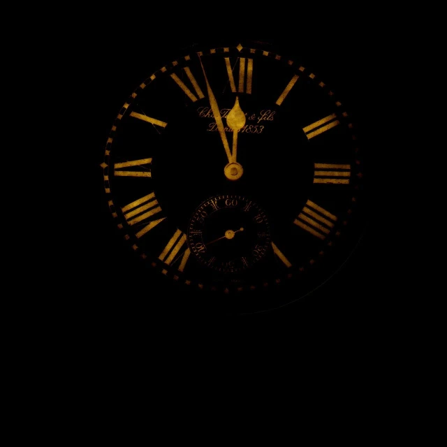 a black and gold clock face is illuminated by yellow hands
