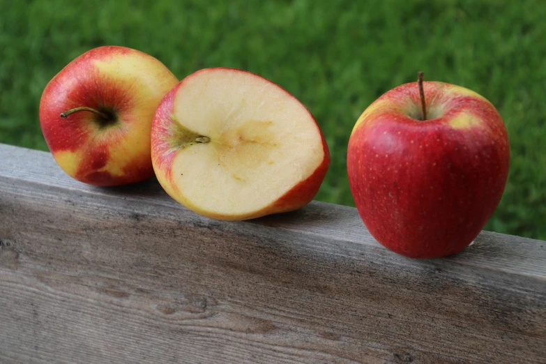 some red and yellow apples sit on a wooden ledge