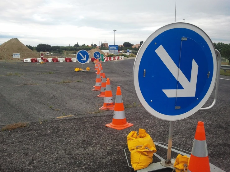 there is an arrow sign and orange cones in the road